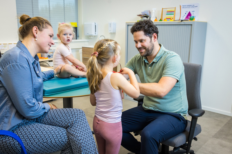 Jeugdarts onderzoekt kind en moeder zit ernaast met zusje